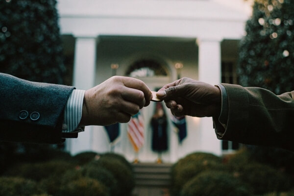 Two individuals exchanging a challenge coin in front of a government building.