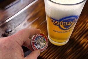 A hand holding a challenge coin next to a glass of beer.