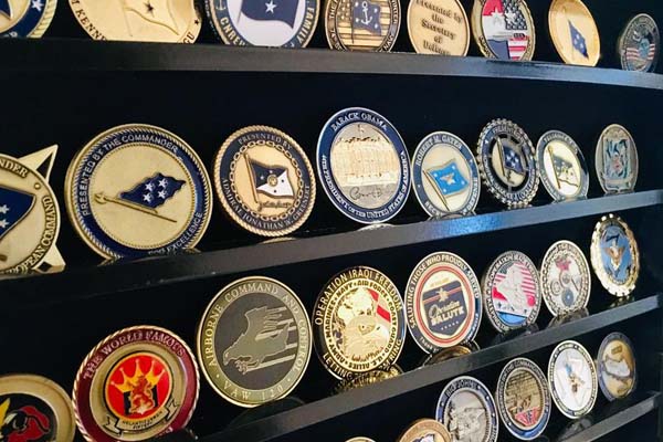 A collection of challenge coins neatly arranged in a wooden display cabinet.